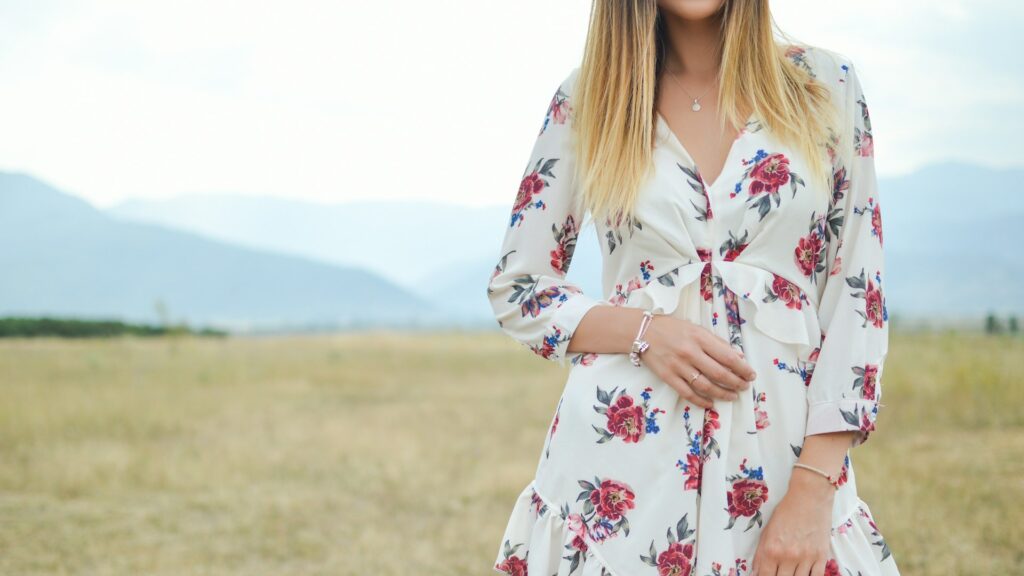 Vrouw met hoed in gele bloemenjurk met diepe uitsnede, staand in een groen veld