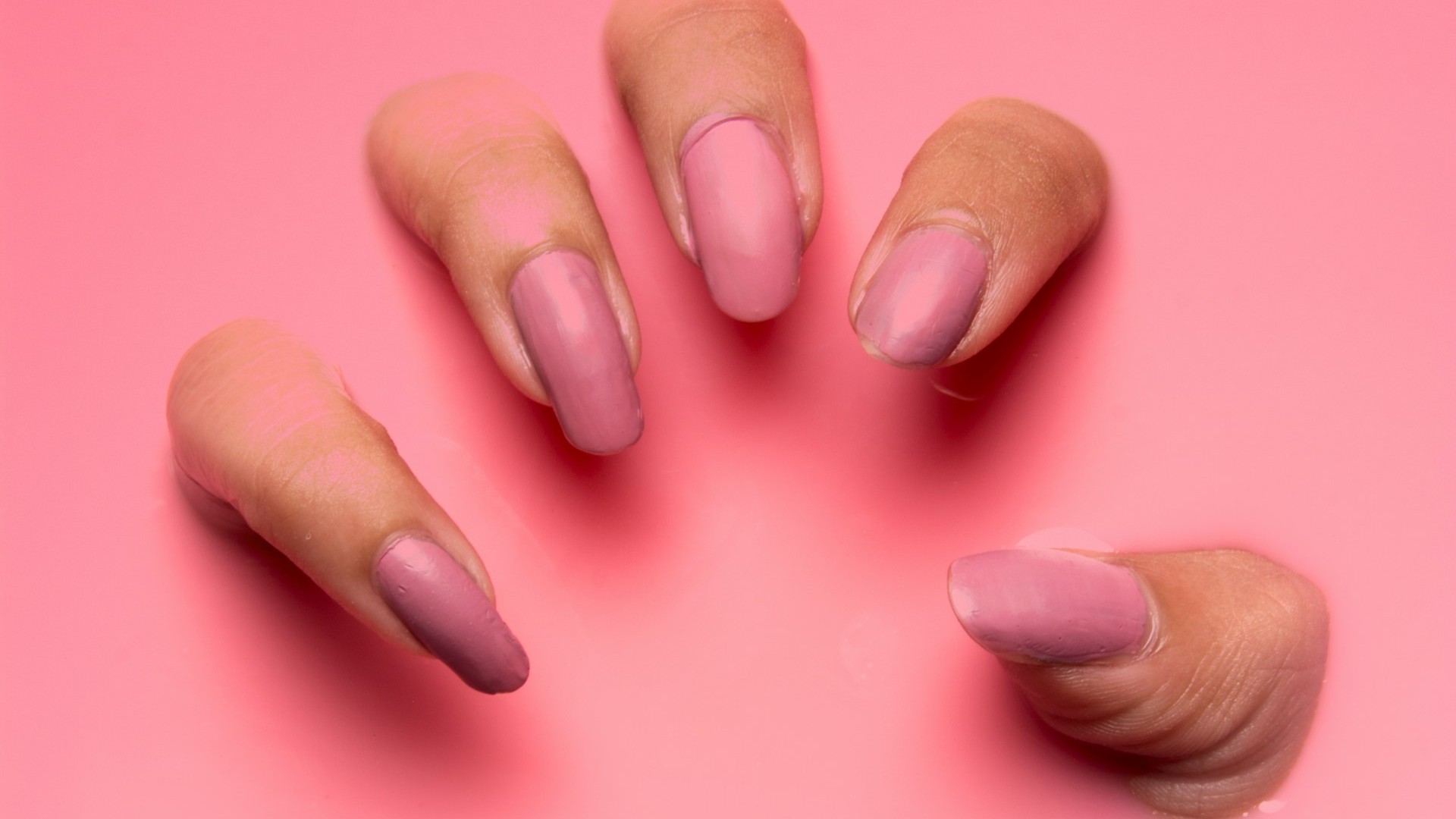 Sterke nagels met roze nagellak op verzorgde handen tegen een roze achtergrond